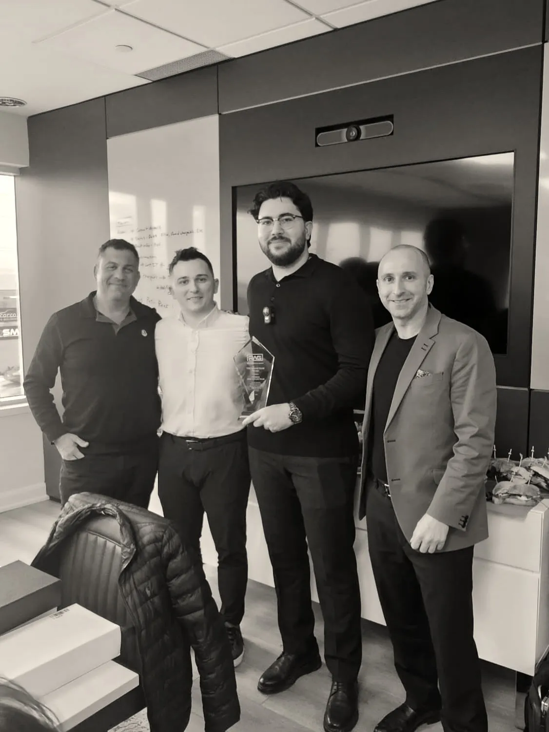 Four men stand in a meeting room at Realty Wealth Group’s Newmarket office; one holds the glass Dream Team trophy.